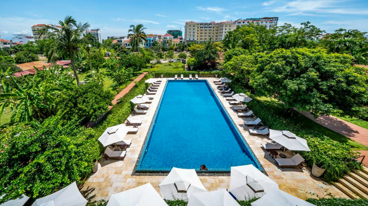 Luxurious resort swimming pool with sunbeds and lush tropical trees in Hoi An, Vietnam.